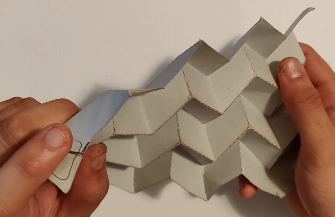 Small scale paper mockup of the origami pattern stretched by two hands