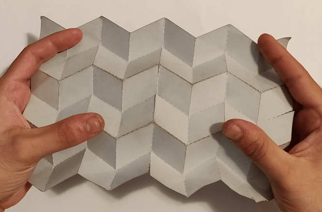 Small scale paper mockup of the origami pattern stretched by two hands